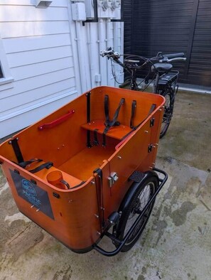 Ein Rollstuhl mit Stauraum, ein Fahrrad und ein Gebäude im Hintergrund.
