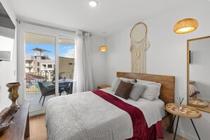 Quarto com cama, mesa de cabeceira, espelho e vista para área externa.