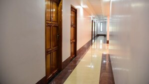A corridor with wooden doors and a polished floor. - Hotel Chembiyan (Pudukkottai)