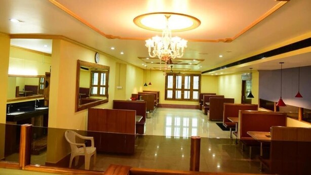 A hotel lobby with a chandelier, seating areas, a mirror, and a view of the outside. - Hotel Chembiyan (Pudukkottai)