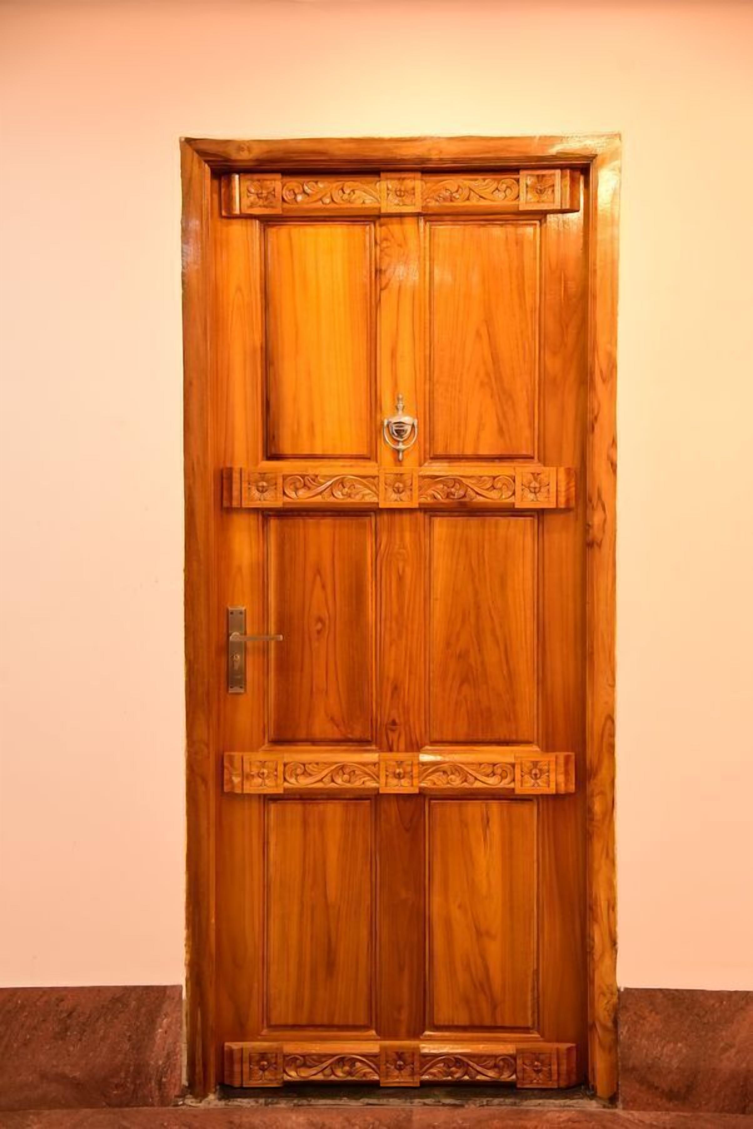 A wooden double door with intricate carvings and a metal handle.