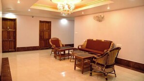 A spacious room with a chandelier, wooden furniture, and a fan on the wall. - Hotel Chembiyan (Pudukkottai)
