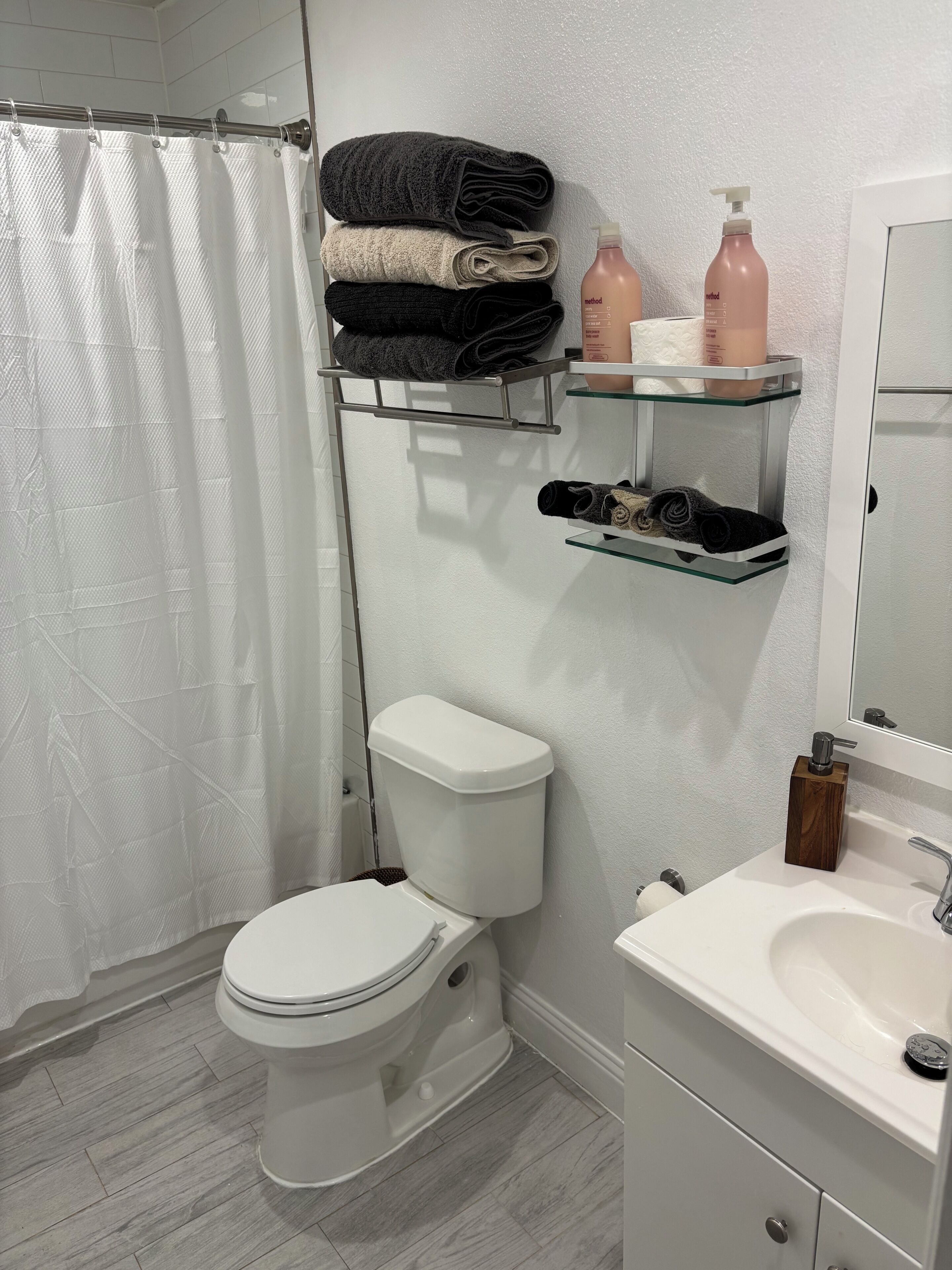 Un baño con inodoro, repisa de vidrio con artículos de aseo y cortina de ducha.