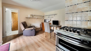 A kitchen with a gas stove, a dining area with a chair, a television, and a wooden door. - Studio Retreat Sleeps 1 - Wifi & Parking (Cambridge)