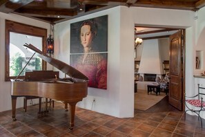 A grand piano in a spacious room with a large painting, wooden ceiling beams, and a view through an open door. - Indian Canyons Golf Resort Fairway-Front Home Pool & Spa + Golf & Mountain Views (Palm Springs)