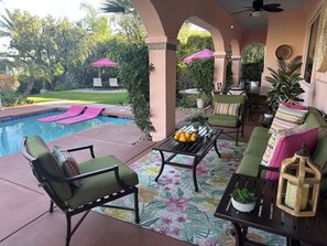 Un área junto a la piscina con sillas de descanso, una mesa con fruta y sombrillas.