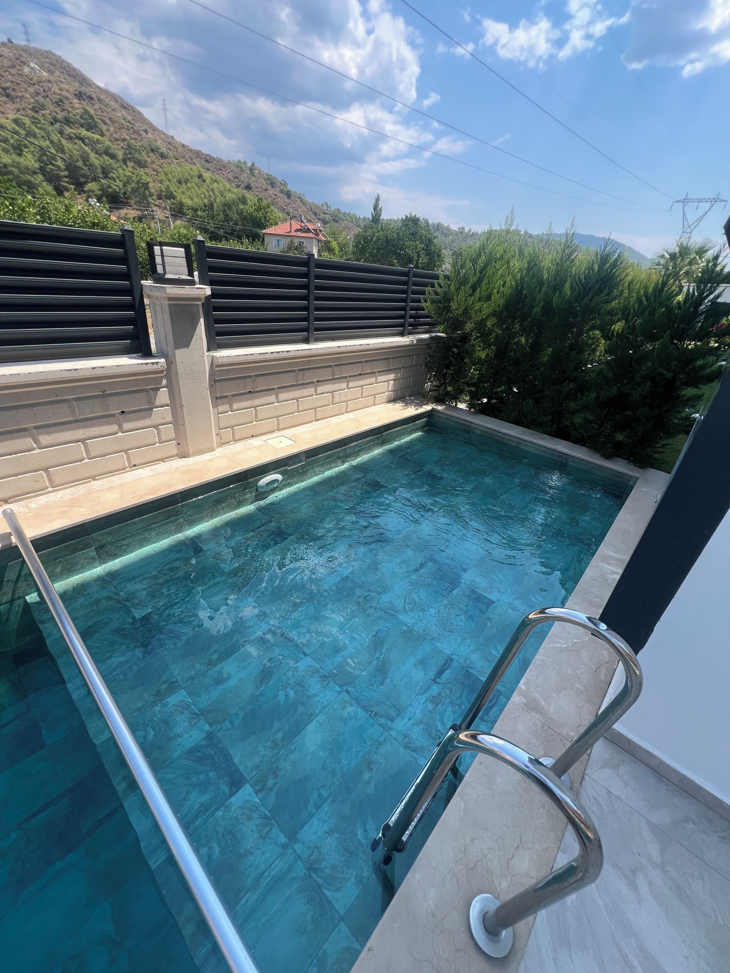 Una piscina de agua cristalina, rodeada por un muro de ladrillo y una barandilla metálica.