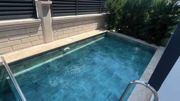 Una piscina de agua cristalina, rodeada por un muro de ladrillo y una barandilla metálica.