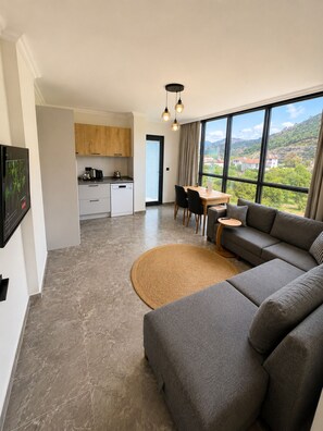 Una sala de estar moderna con un sofá gris, una mesa de comedor y una cocina al fondo.