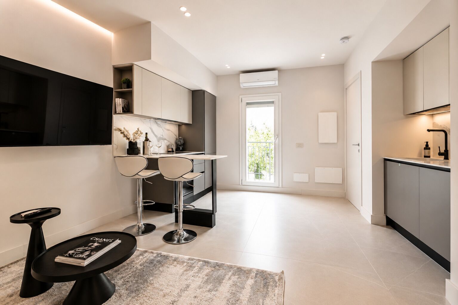 Una cucina moderna con forno integrato, un'area pranzo con due sgabelli da bar, una TV a schermo piatto montata a parete e un'ampia finestra che offre luce naturale.