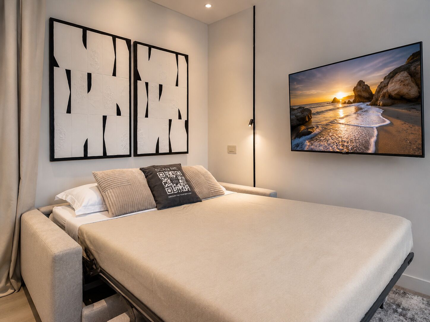 Una camera da letto moderna con un letto, una TV a parete, opere d'arte astratte e vista su un tramonto sulla costa.