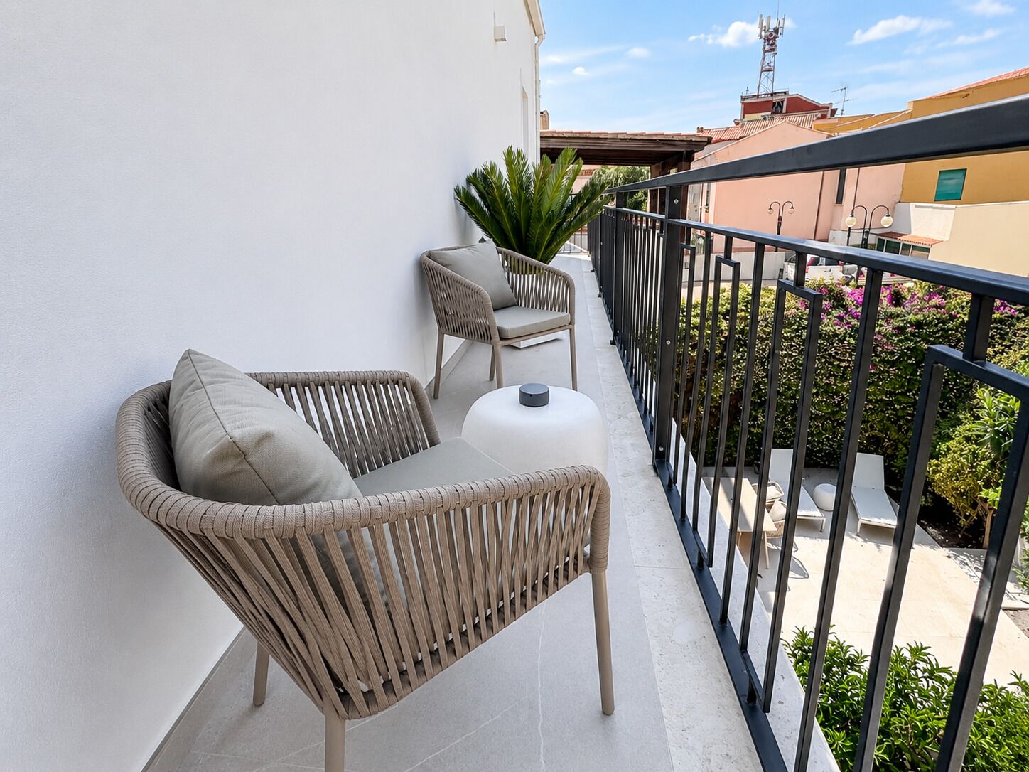 Un balcone con mobili in vimini, un tavolo bianco e una pianta in vaso.