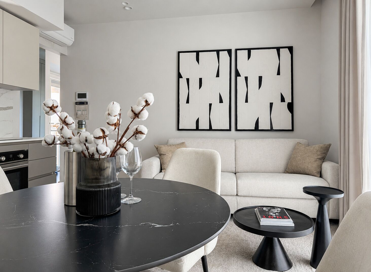 A modern living room with a sofa, a round table, and a coffee table. There is a vase with cotton branches on the table.