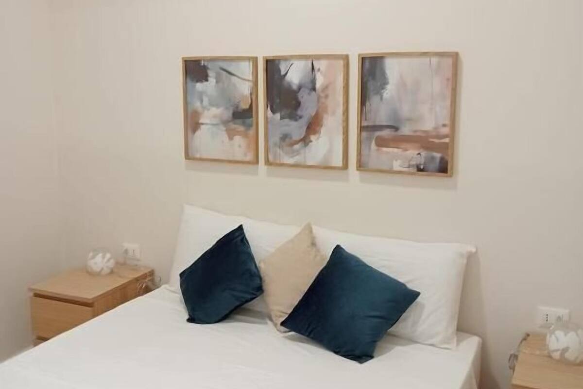 Un dormitorio con una cama, dos mesitas de noche y tres cuadros abstractos en la pared.