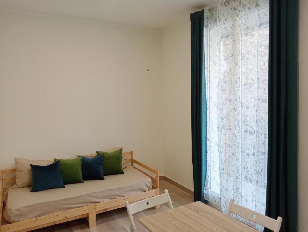 A small room with a single bed, a table, and a window with curtains.