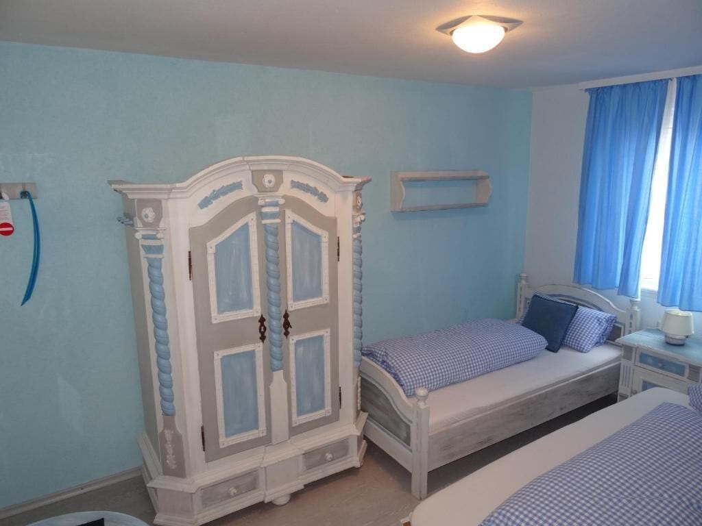 Un dormitorio con cama, armario, mesita de noche y ventana con cortinas.