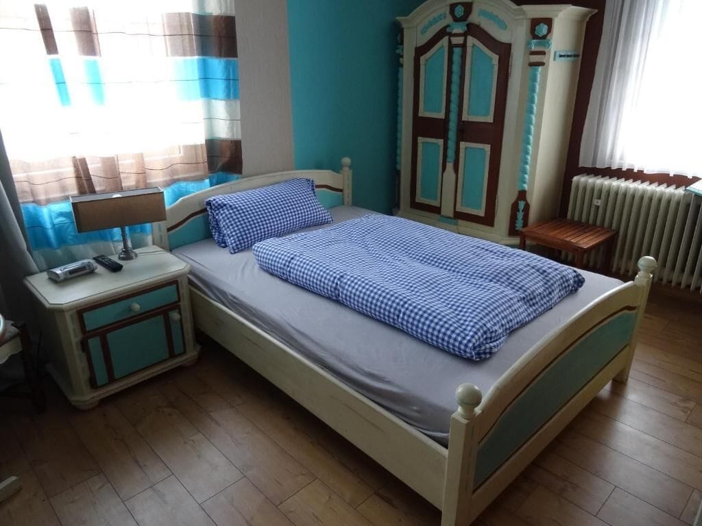 Un dormitorio con cama, mesita de noche, armario y ventana con cortinas.