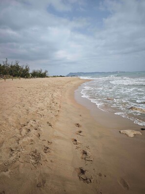 A sandy beach with footprints, a wooden fence, and a distant cityscape.