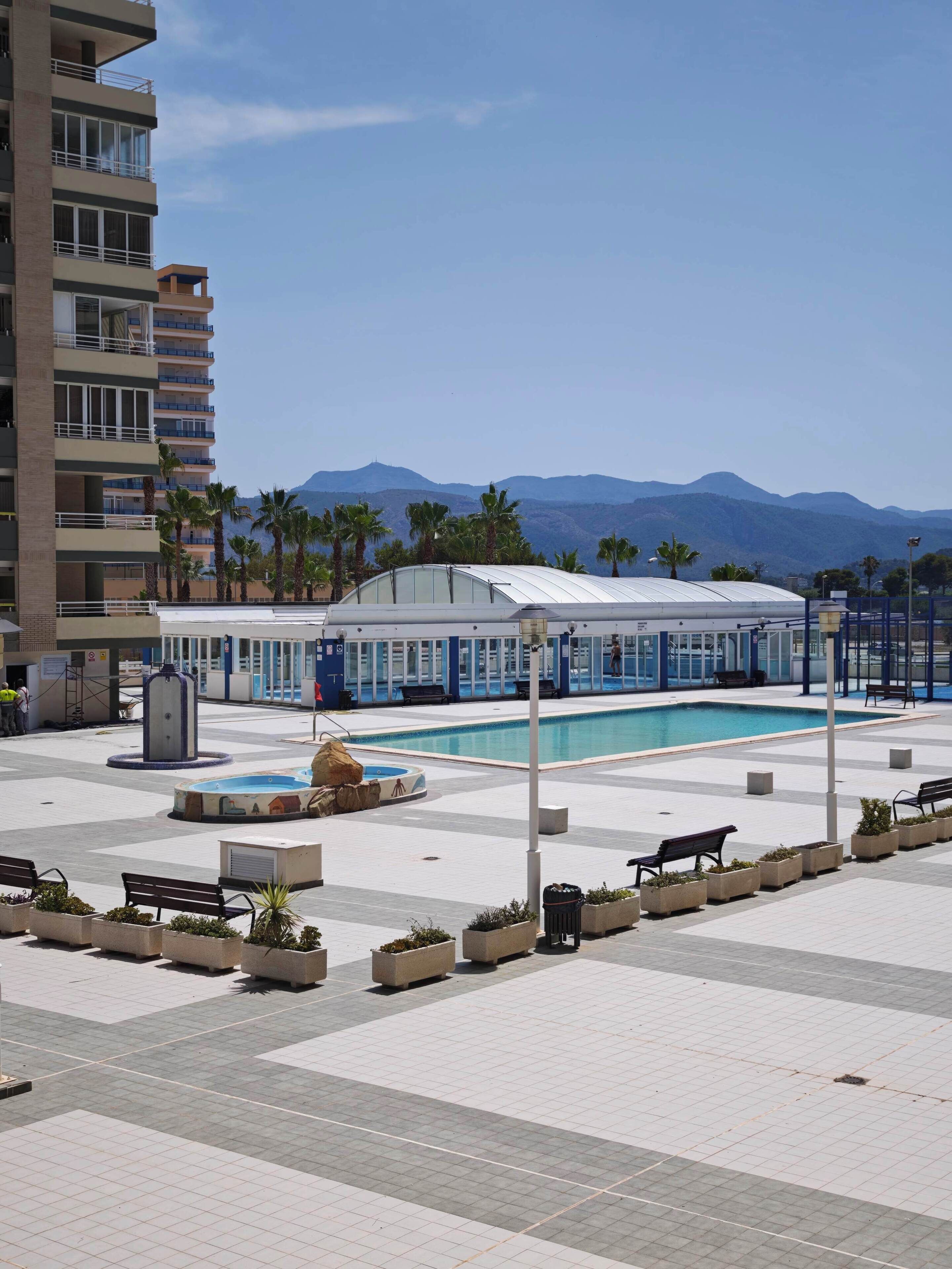 A hotel with a swimming pool, outdoor seating, and a view of mountains.