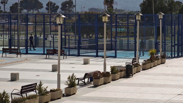 A spacious outdoor area with a tennis court, benches, and street lamps.