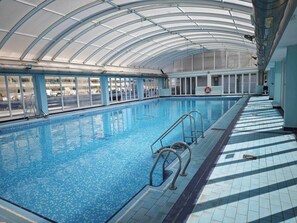 An indoor swimming pool with clear glass walls, metal railings, and a tiled floor.