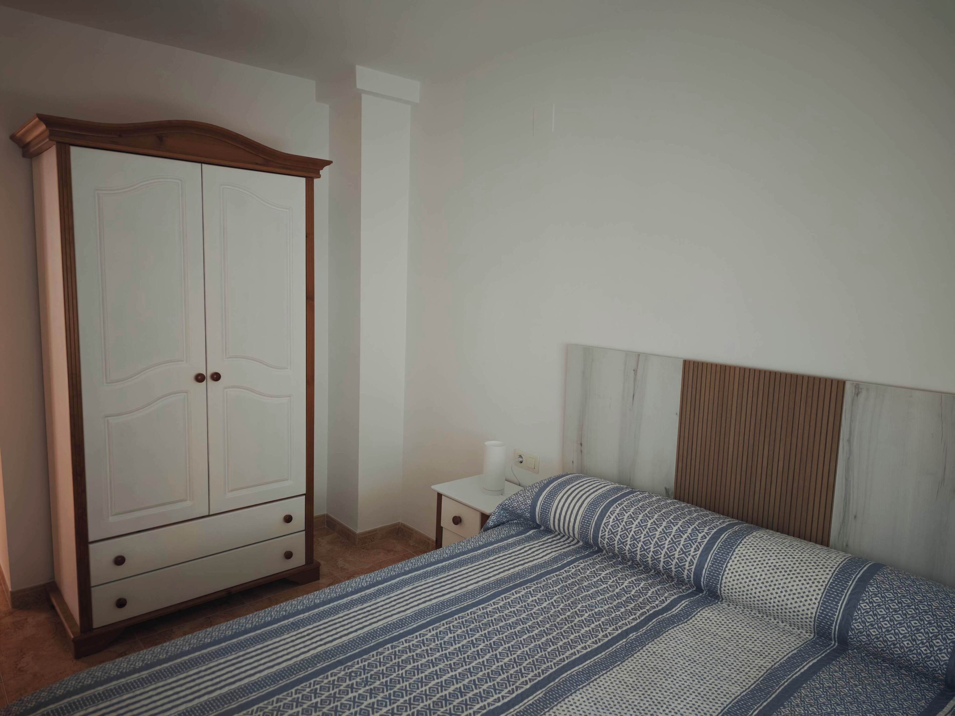 Un dormitorio con cama, armario, mesita de noche y estante en la pared.