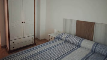 Un dormitorio con cama, armario, mesita de noche y estante en la pared.