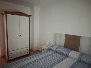 A bedroom with a bed, a wardrobe, a nightstand, and a wall-mounted shelf.