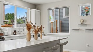 Une cuisine moderne dotée d’un grand îlot central, de meubles blancs et offrant une vue sur le jardin arrière.