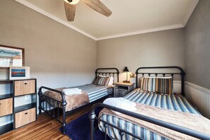 A bedroom with two single beds, a wooden shelf unit, a ceiling fan, and a framed picture on the wall.