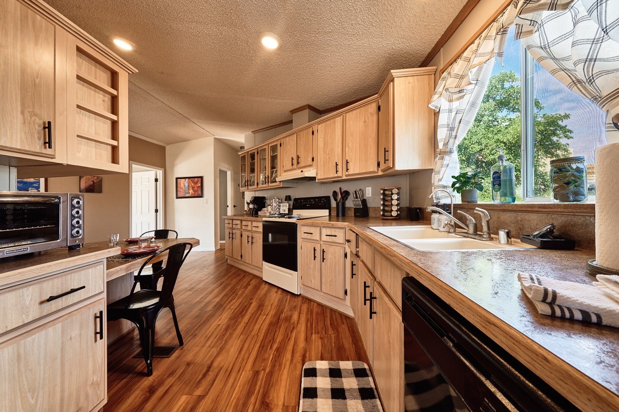A kitchen with wooden cabinets, a built-in oven, a dishwasher, and a window with a view of greenery.