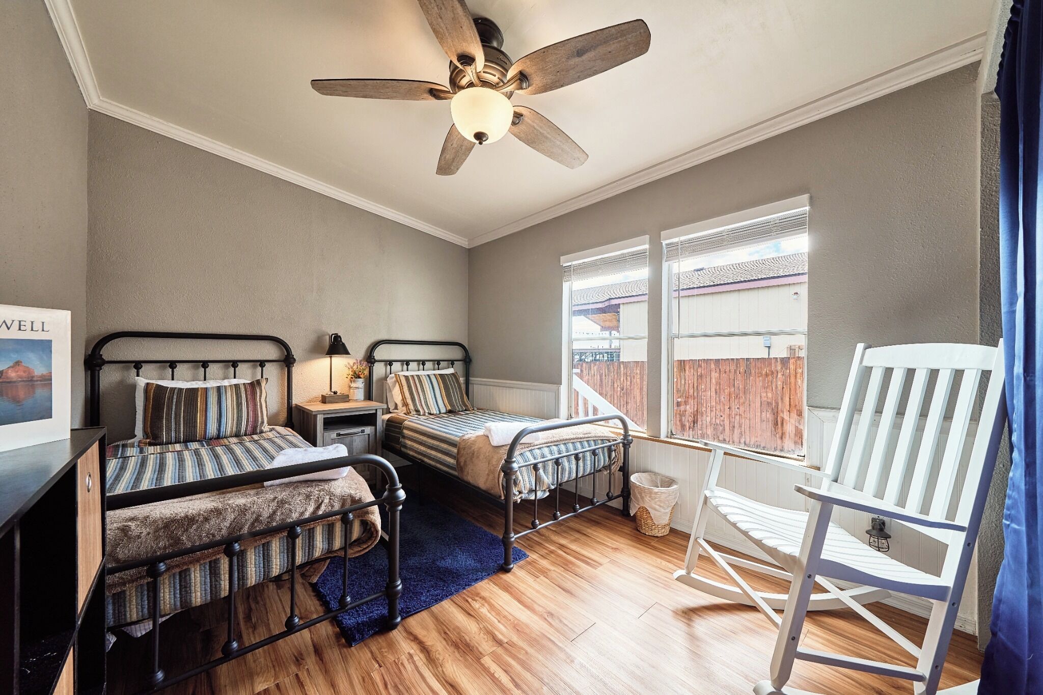 A bedroom with two beds, a ceiling fan, a window with a view, and a rocking chair.