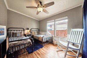 Un dormitorio con dos camas, un ventilador de techo, una ventana con vistas y un sillón mecedora.