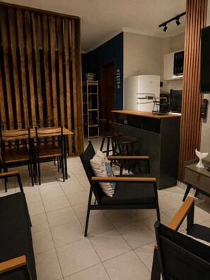 A modern kitchen with a bar area, wooden furniture, and a tiled floor. - Kitnet na Ocian - 500 metros do mar, Ar condicionado  e garagem (Praia Grande)