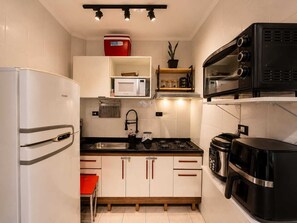 A compact kitchen with a refrigerator, microwave, stove, and coffee maker. - Kitnet na Ocian - 500 metros do mar, Ar condicionado  e garagem (Praia Grande)