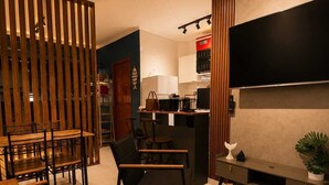 Ein modernes Wohnzimmer mit einer Couch, Sesseln, einem Fernseher, einer Küchenzeile und einer Holzwand.