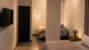 Habitación de hotel moderna con una cama grande, un televisor montado en la pared y una zona de descanso separada con un sofá.