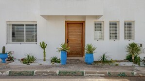 Ein Gebäude mit einer Holztür, weißen Wänden und blauen Pflanzgefäßen mit Pflanzen.