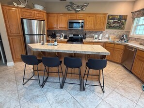 A kitchen with wooden cabinets, a stainless steel refrigerator, a microwave, a stove, and a large island with bar stools. - Grand Lake Retreat, Two Decks with Stunning Views (Grove)