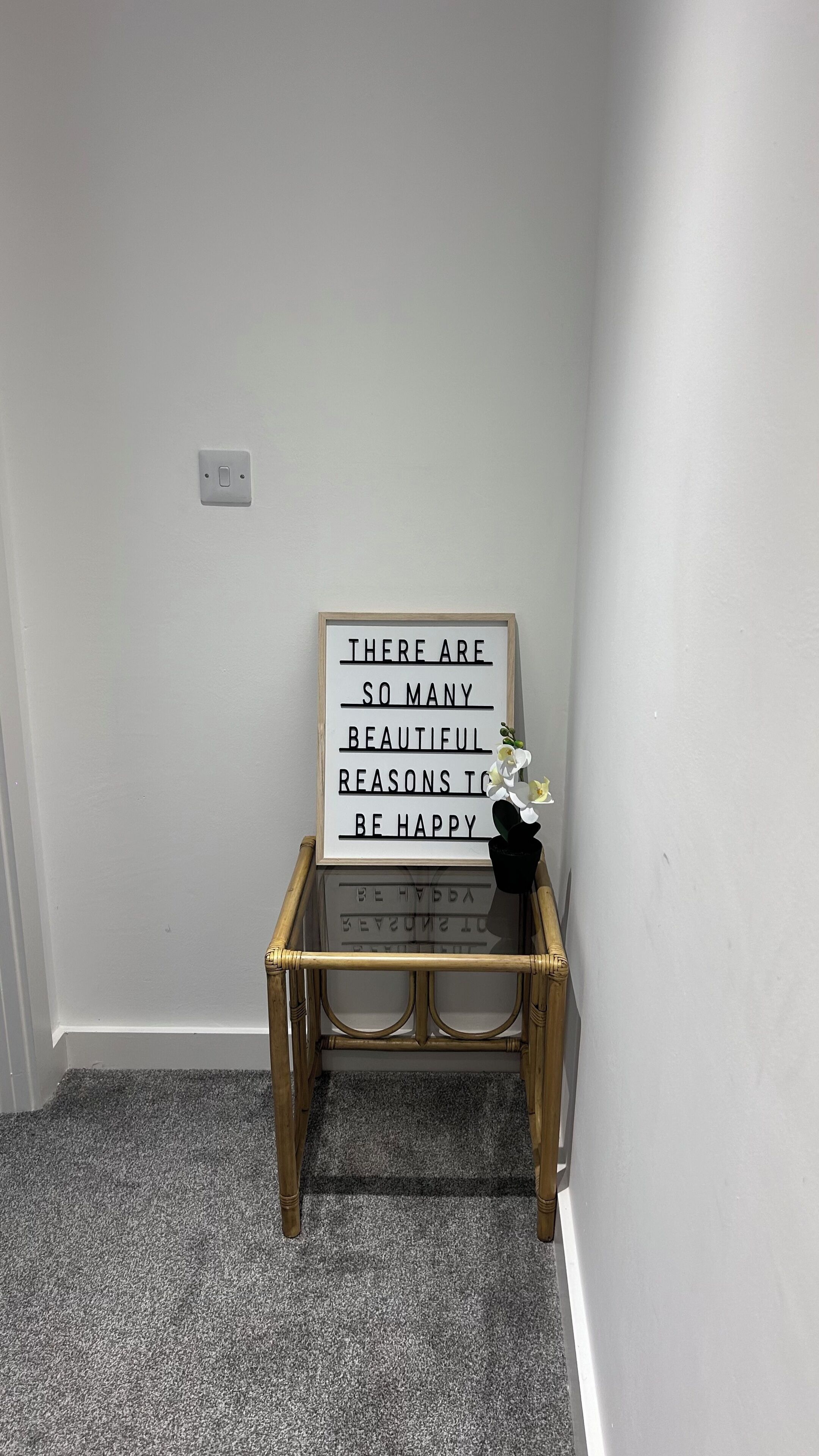 A corner with a small wooden table, a lightbox sign, and a vase with flowers.
