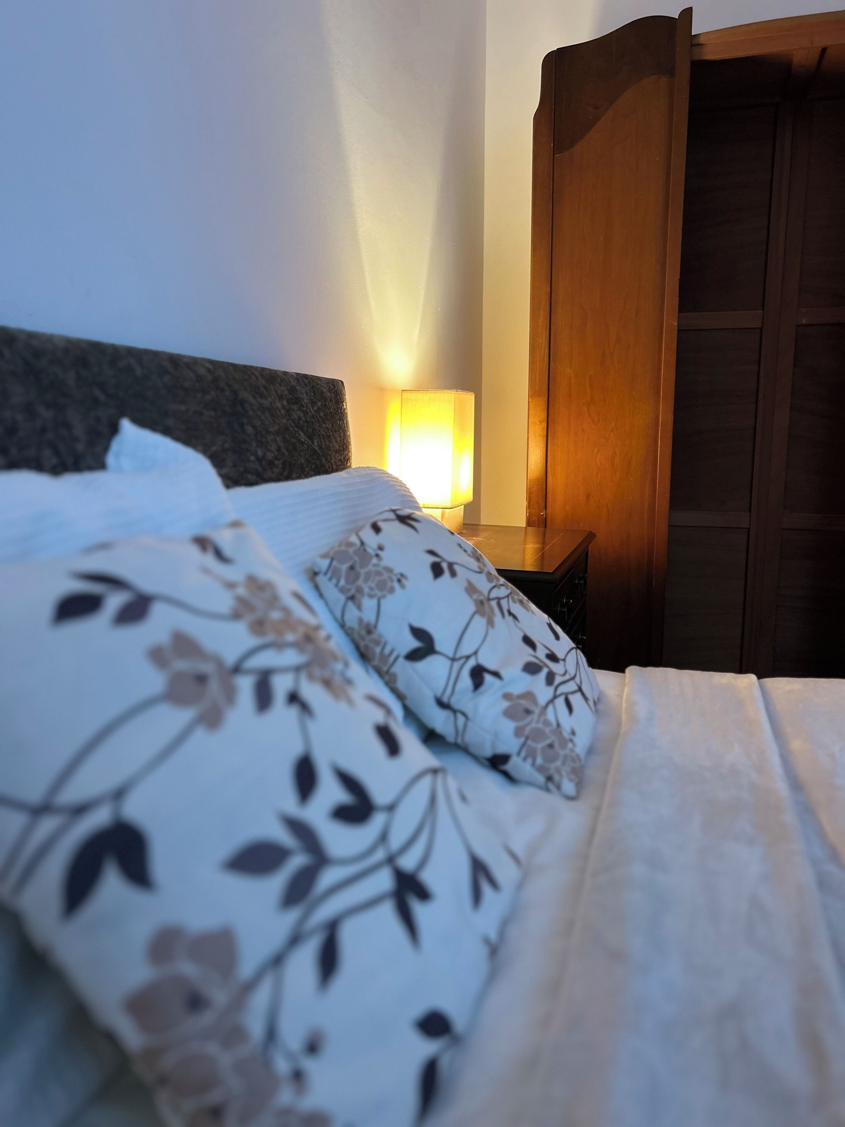 Een bed met bloemenbeddengoed, een bedlampje en een houten garderobe.