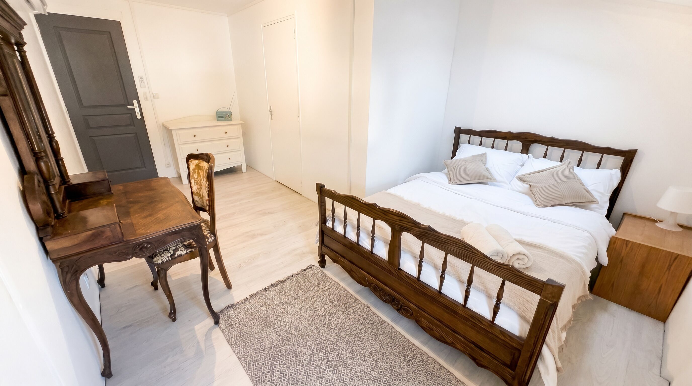 Um quarto com cama de madeira, escrivaninha, cadeira e cómoda.