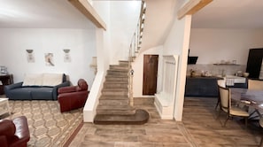 Una escala que condueix a un segon pis, un saló amb un sofà i una catifa amb dibuixos, i una cuina amb taula de dinar.