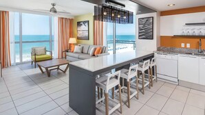 Una habitación de hotel moderna con un balcón grande, un área de cocina y un espacio de descanso con vista al océano.