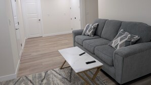 A living room with a grey sofa, a white coffee table, and a patterned rug. - New Cozy 2 Bedrooms Basement Apartment (Calgary)