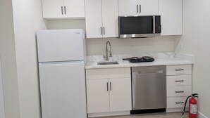 A compact kitchen with white cabinets, a stainless steel refrigerator, a microwave, a sink, and a dishwasher. - New Cozy 2 Bedrooms Basement Apartment (Calgary)