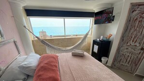 A hotel room with a bed, pillows, a hammock, a view of the sea, a Netflix sign, and a door with a decorative pattern. - Azul Hotel Boutique (Santa Marta)