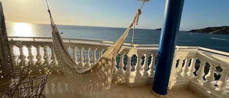 A balcony with a hammock, white balustrade, and a view of the sea.