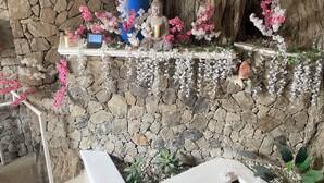 A stone wall with a shelf holding a Buddha statue, candles, and pink flowers. - Azul Hotel Boutique (Santa Marta)
