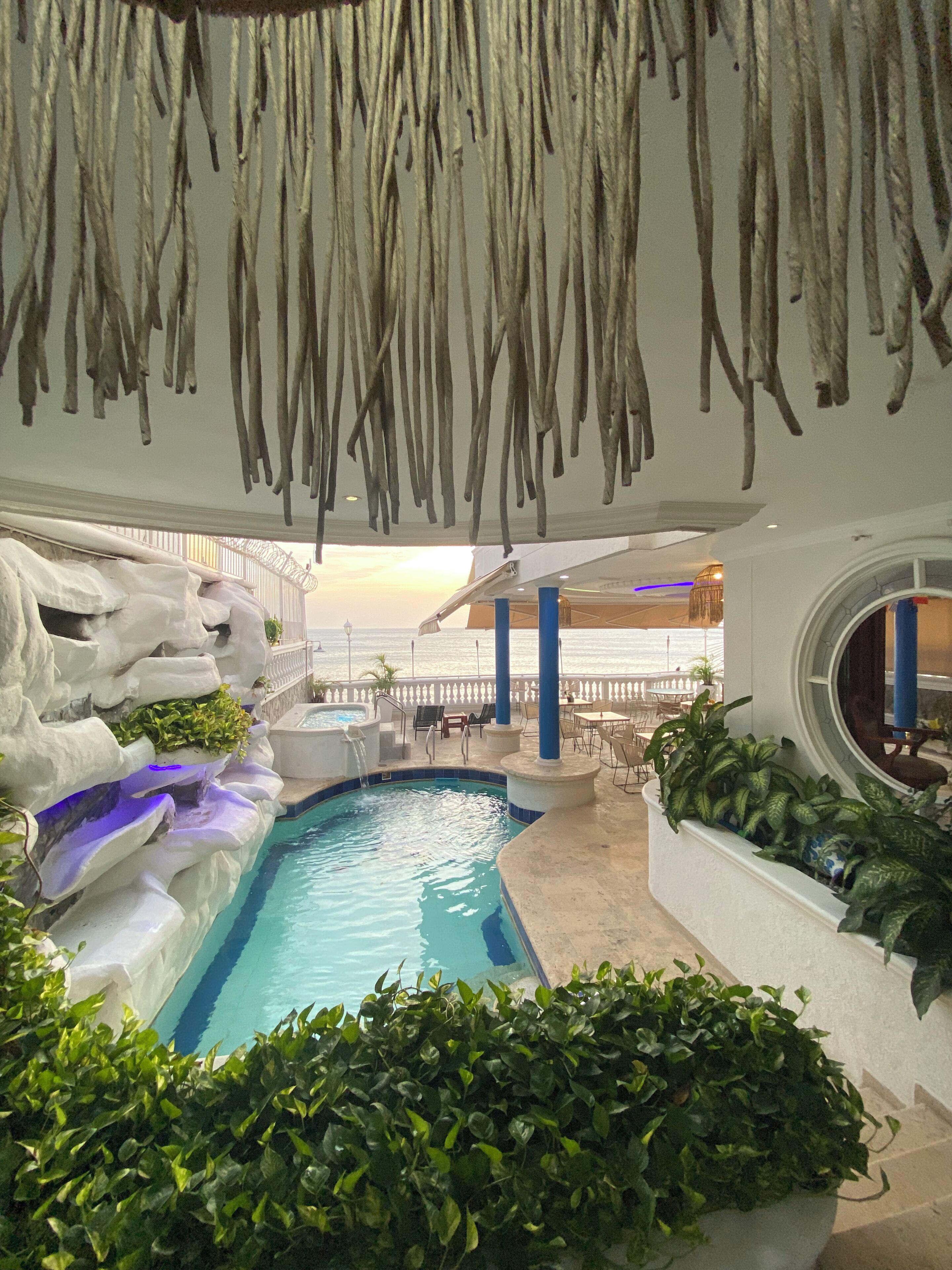 Un área de piscina interior con vistas al mar, rodeada de formaciones rocosas y plantas.